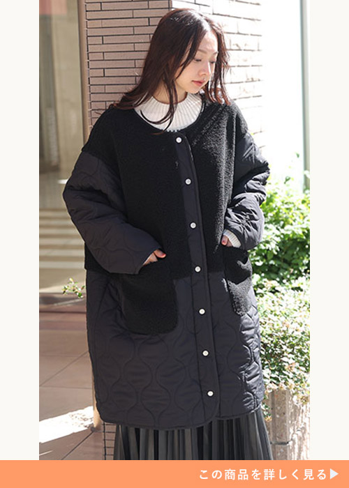 ひょうたんデザインのキルティングとボア素材のブラックノーカラーコートに、プリーツスカートを履く女性