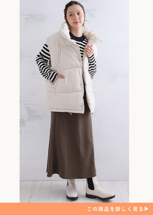 ホワイトのフェイクダウンオーバーベストにボーダーニットとブラウンスカートを履く女性