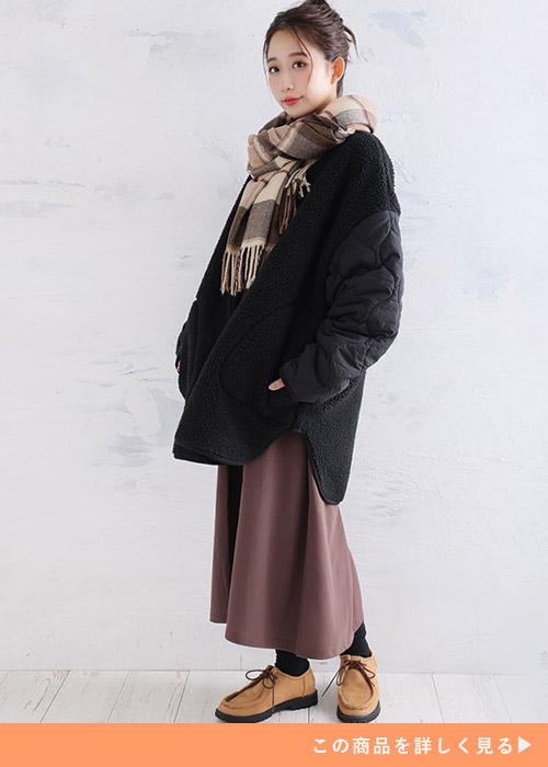 ブラックの袖キルトのボアジャケットにブラウンチェックのストールとくすみカラースカートを合わせる女性