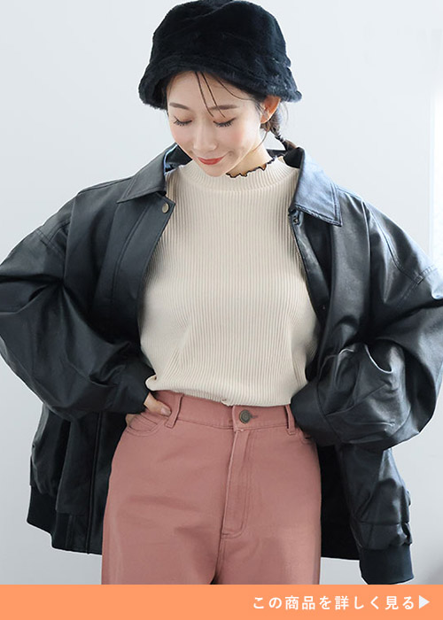 ホワイトニットとカラーパンツのコーデにブラックのフェイクレザービッグジャケットを羽織る女性