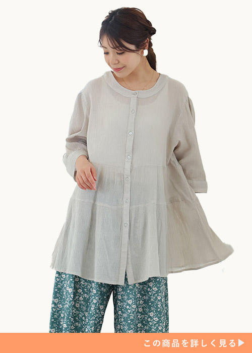 ライトベージュのシアーブラウス×グリーンの花柄パンツを着る女性