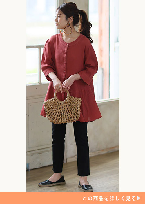 シアー素材のオレンジ色ティアードブラウス×黒のスキニーパンツを着る女性