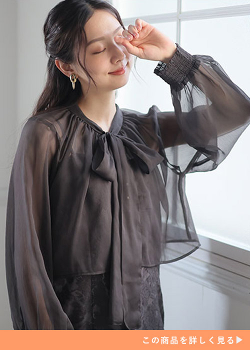 ブラックのレースキャミワンピースにシースルーのリボン付きブラウスをレイヤードする女性