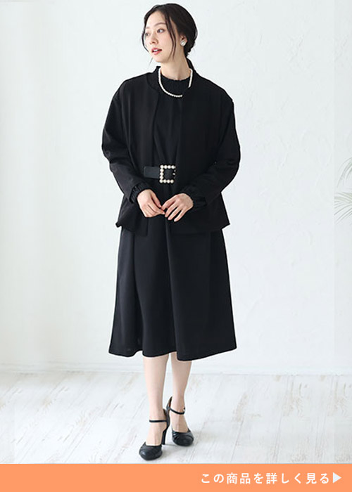 ブラックのAラインワンピースとブラックジャケットのコーデにベルトでウエストマークする女性
