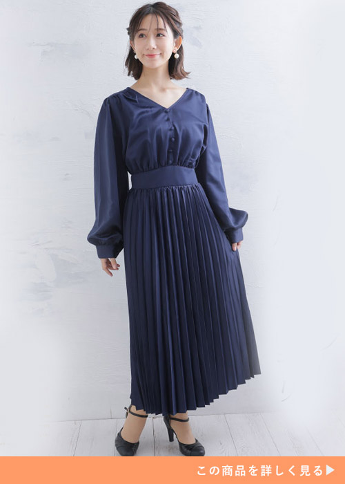 ネイビーの肩タックプリーツワンピースにブラックのストラップパンプスを履く女性