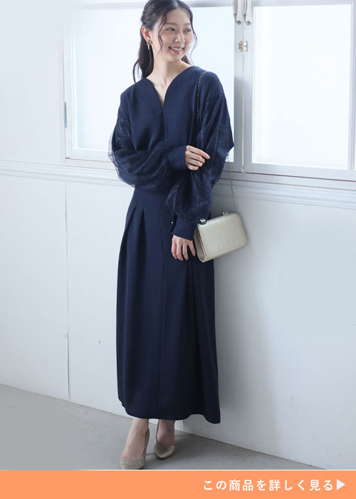 ネイビーの袖チュールワンピースにゴールドのバッグとパンプスを合わせる女性