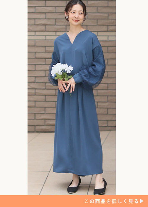 ブルーの袖チュールワンピースにブラックのフラットシューズを履く女性