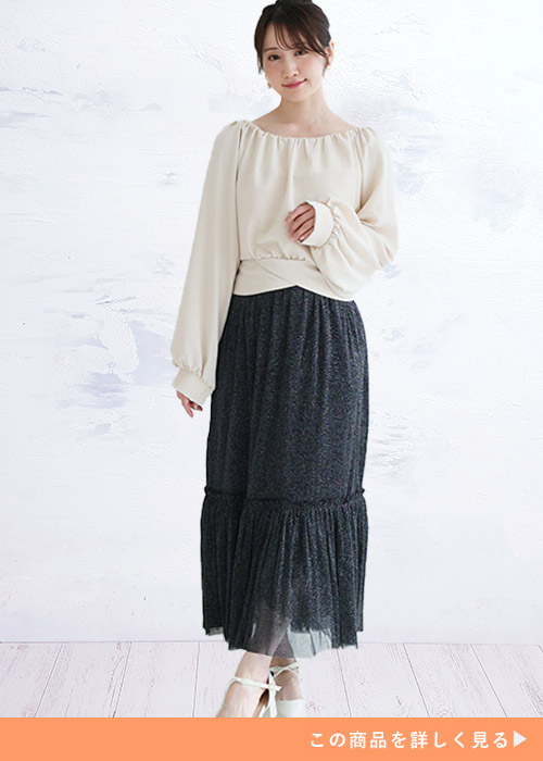 アイボリーのトップスとラメチュールのブラックティアードスカートを履く女性
