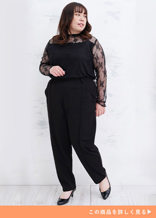 ブラックのテーパードパンツにレースデザイントップスを合わせ、黒パンプスを履く女性