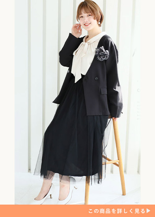 ブラックのショート丈ダブルボタンジャケットに白のブラウスと黒のレーススカートを履く女性