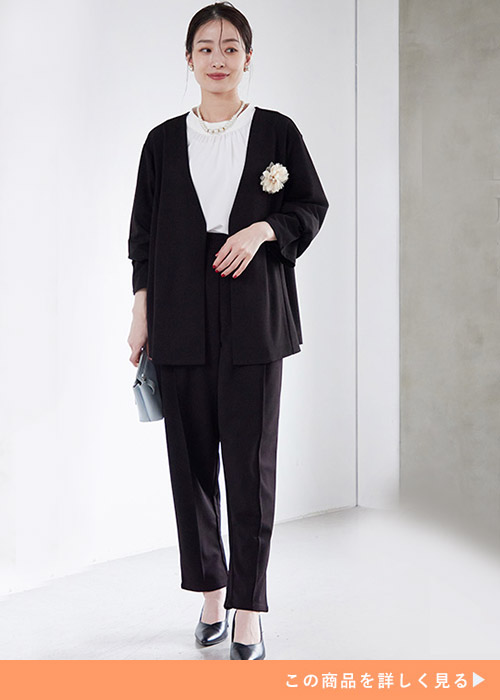 ブラックジャケットのパンツスーツとホワイトのブラウスを着る女性