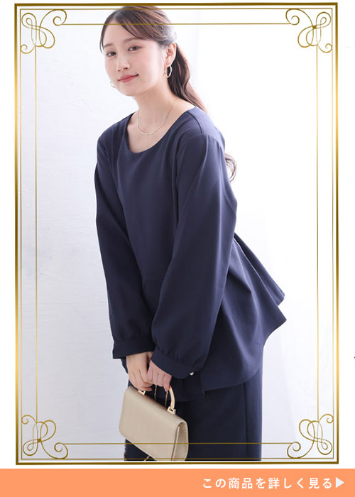 ネイビーのペプラムトップスとパンツのセットアップにベージュのバッグを持つ女性