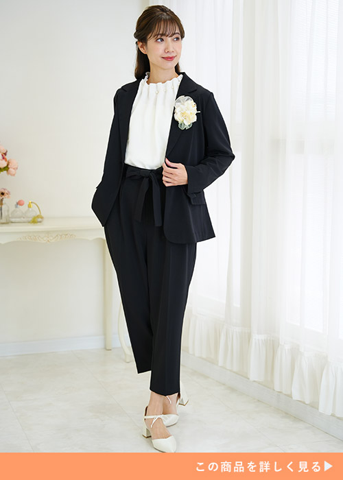 ブラックジャケットのパンツスーツにホワイトのブラウスとパンプスを合わせる女性