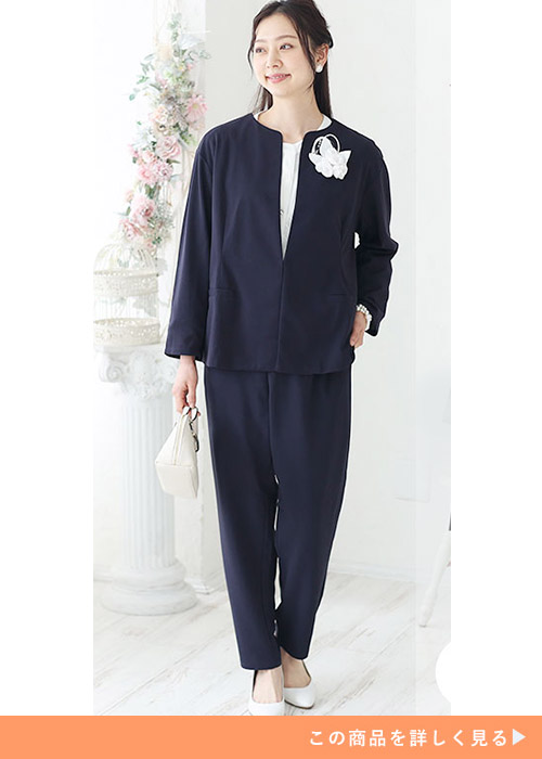 ネイビーのノーカラージャケットのパンツスーツにホワイトのブラウスを合わせる女性