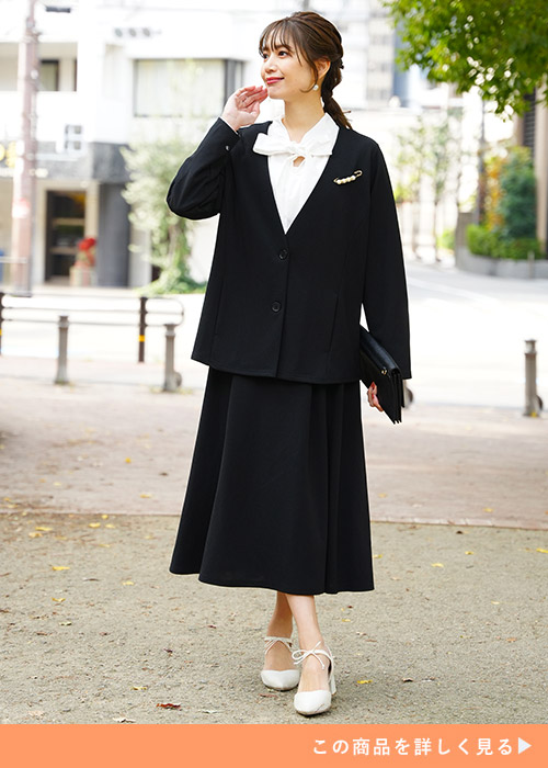 ブラックのジャケットとスカートのスーツにホワイトのブラウスとパンプスを合わせる女性