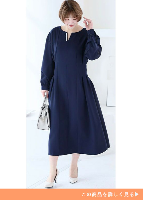 ネイビーのパールモチーフワンピースに白のパンプスとバッグを合わせる女性