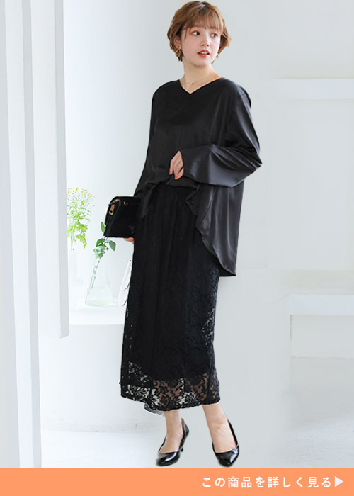 レースとサテンのブラックドッキングレースワンピにパンプスとバッグを合わせる女性