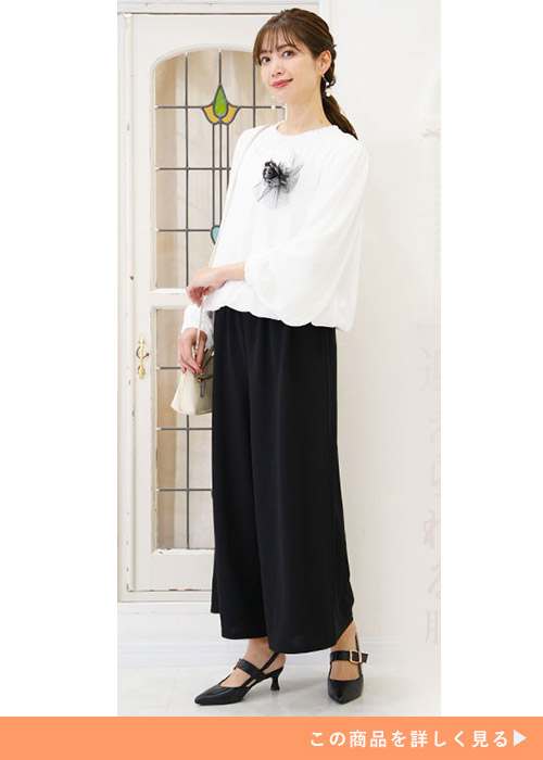 ホワイトブラウスとブラックワイドパンツのセットアップにブラックパンプスを履く女性