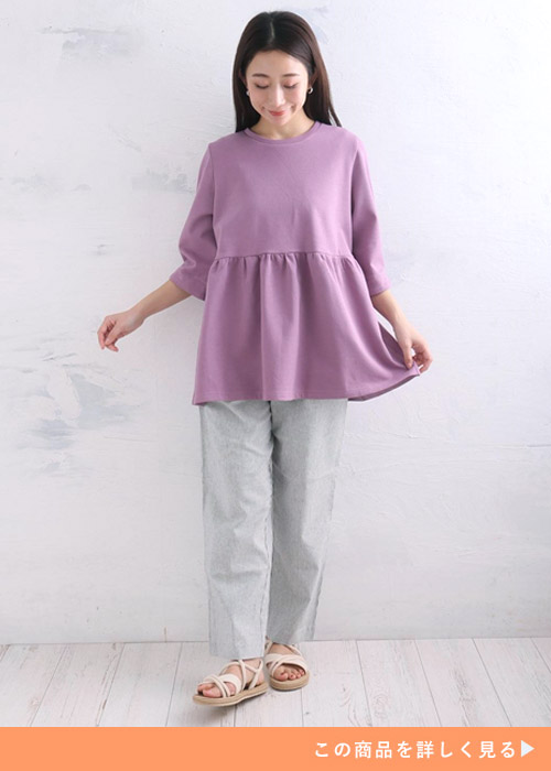 ラベンダー色の「ハッピーさらりん」ペプラムトップス×グレーのパンツを着る女性