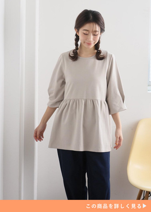 ベージュのペプラムトップス×デニムパンツを着る女性