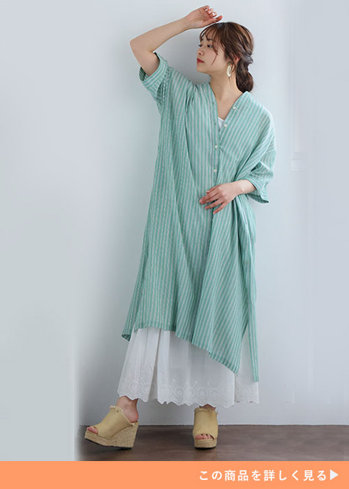 グリーンのストライプ柄シャツワンピースの下に、レーススカートを重ね着する女性