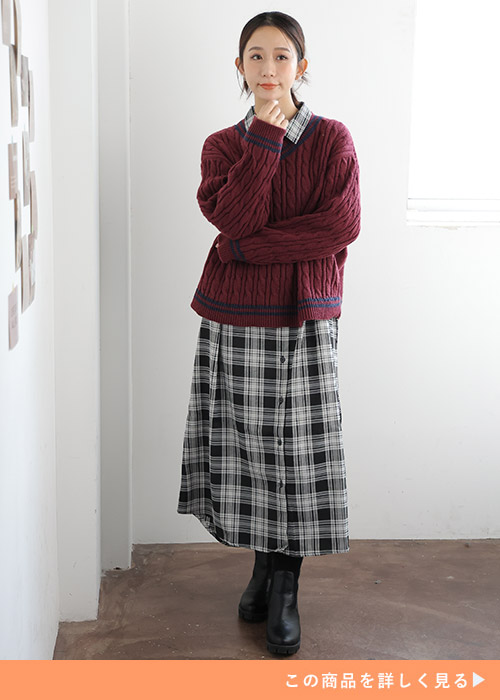 モノトーンチェック柄のシャツワンピースの上に、ボルドーのニットを重ね着する女性