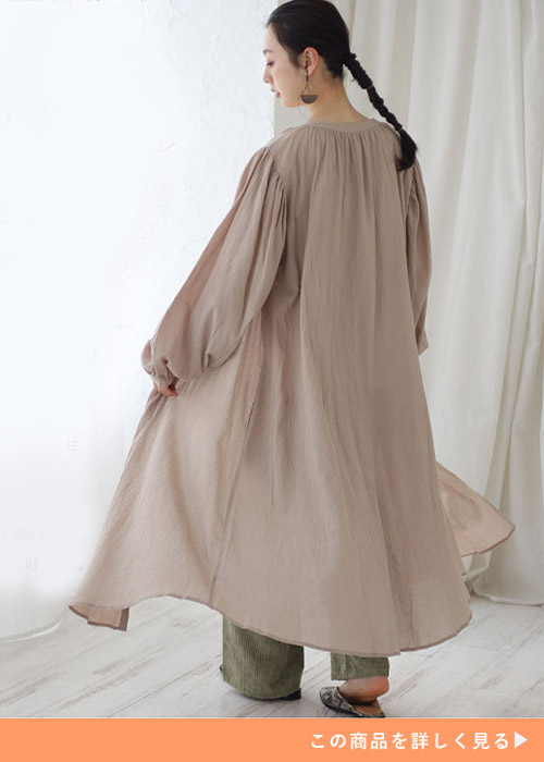 パンツルックに前ボタンを開けたベージュのシャツワンピースを羽織る、後ろ姿の女性