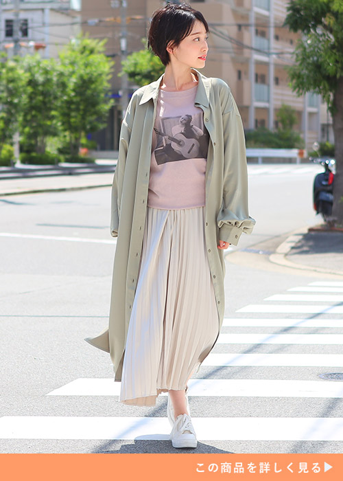 ピンクのTシャツ×白のプリーツスカートに、ボタンを開けたライトグリーンのシャツワンピースを羽織る女性