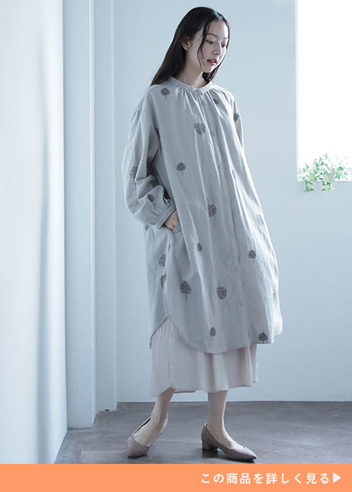 グレージュのツリー柄刺しゅうシャツワンピ×プリーツスカートを着る女性