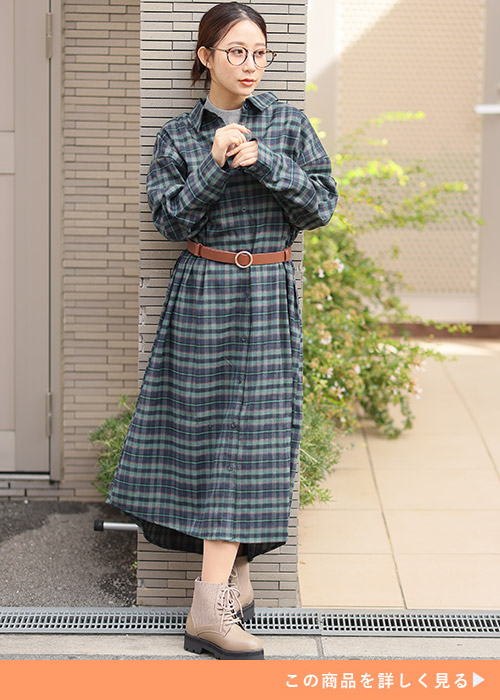 グリーンのチェック柄ワンピースの下にグレートップスを着て、ブラウンのベルトをする女性