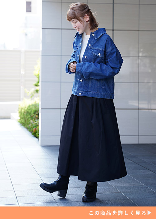 ホワイトニットとブラックスカートのコーデにデニムGジャンを羽織る女性