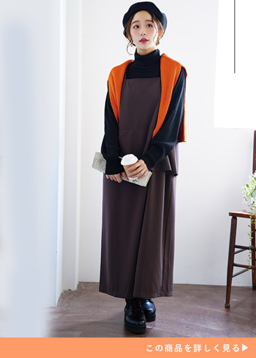 ブラウンのジャンスカとブラックニットトップスのレイヤードにオレンジニットを羽織る女性