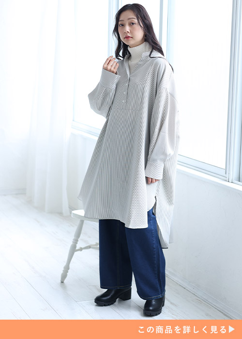 ストライプカーキのバックボタンシャツワンピとニットトップスのレイヤードにデニムパンツを履く女性