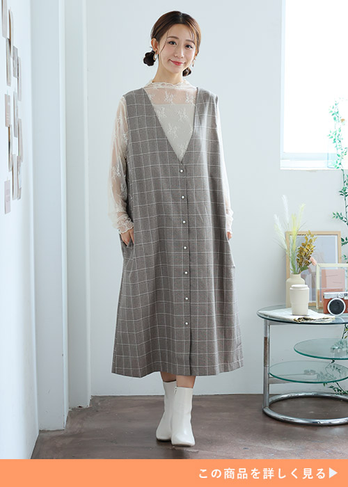 レースのシアートップス×チェック柄のVネックジャンパースカートを着る女性