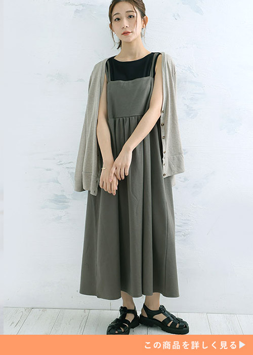 黒のノースリトップス×カーキのジャンパースカートを着て、カーディガンを肩に掛ける女性