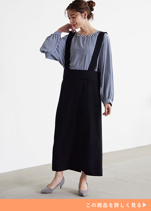 ブルー系ブラウス×黒のジャンパースカートを着る女性