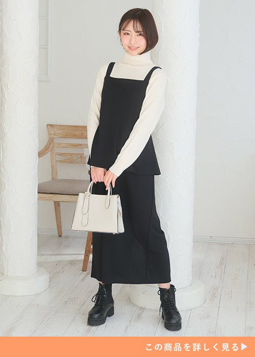 白のタートルネックニット×黒のペプラムデザインジャンパースカートを着る女性