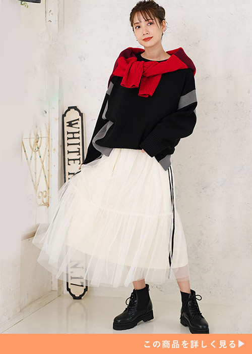 アイボリーのライン入りチュールスカートとブラックトップスのコーデに、レッドカーデを羽織る女性