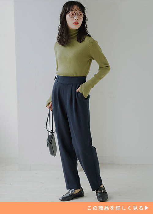 ブラックのテーパードパンツにグリーンのタートルネックトップスを合わせる女性