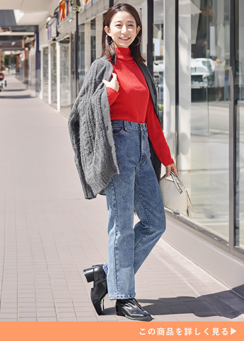 ネイビーケミカルのデニムパンツにレッドニットを合わせ、ケーブル編ニットカーデを羽織る女性