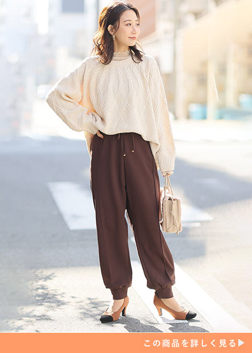 ブラウンのジョガーパンツとアイボリーのニットのコーデにブラウンのパンプスを履く女性