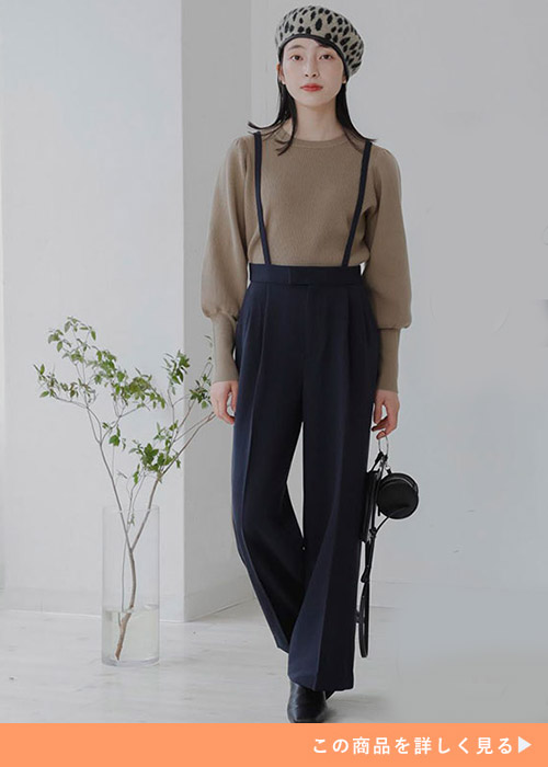 ブラックのサスペンダー付きパンツにブラウンのトップスを合わせる女性