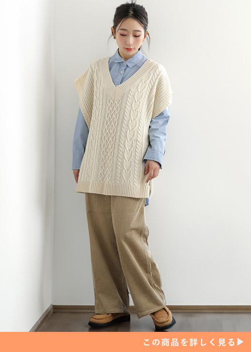 ベージュのコーディロイペインターパンツにシャツとニットのレイヤードを合わせる女性