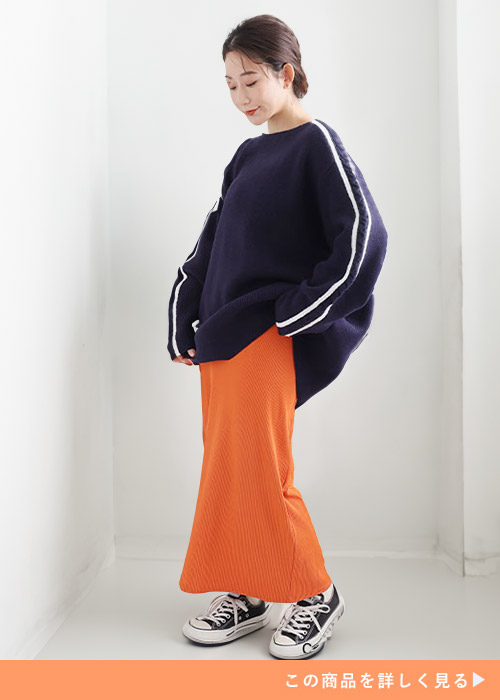 ネイビーの配色ニットトップスとオレンジのスカートのコーデに黒スニーカーを履く女性