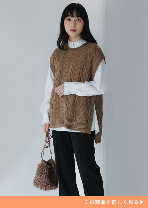 ホワイトフリルシャツにベージュのニットベストをレイヤードし、ブラックのパンツを履く女性