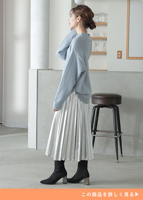シルバーのプリーツスカートとブルーのニットのコーデにブラックブーツを履く女性