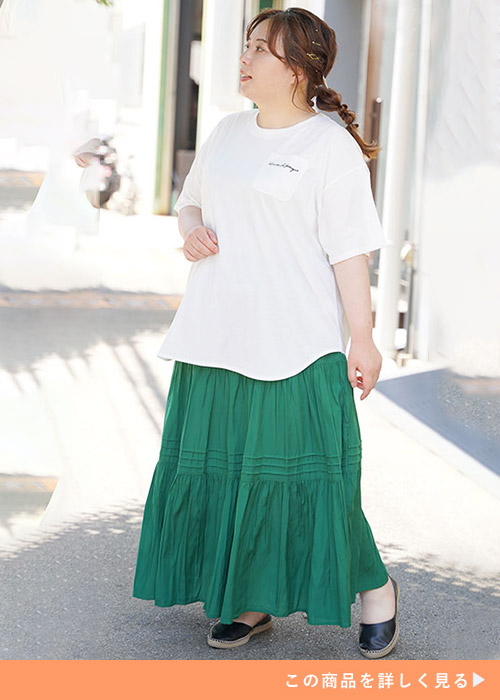 白のチュニック丈Tシャツ×緑のロングスカートを着る女性