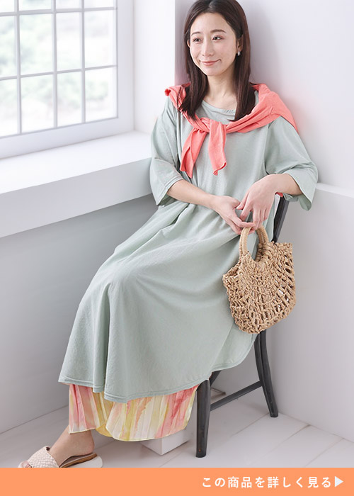 ミントグリーンのワンピースの下にタイダイ柄プリーツスカートを履き、ピンクトップスを肩に巻く女性