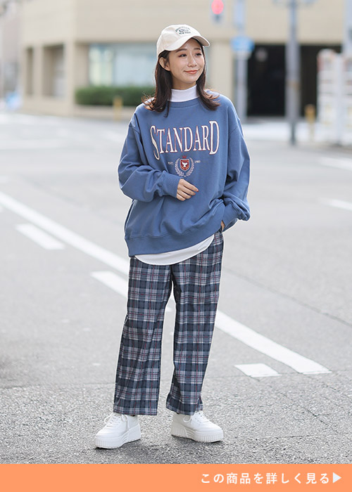 白トップスをのぞかせた水色のロゴスウェット×チャコール色のチェック柄パンツを着る女性