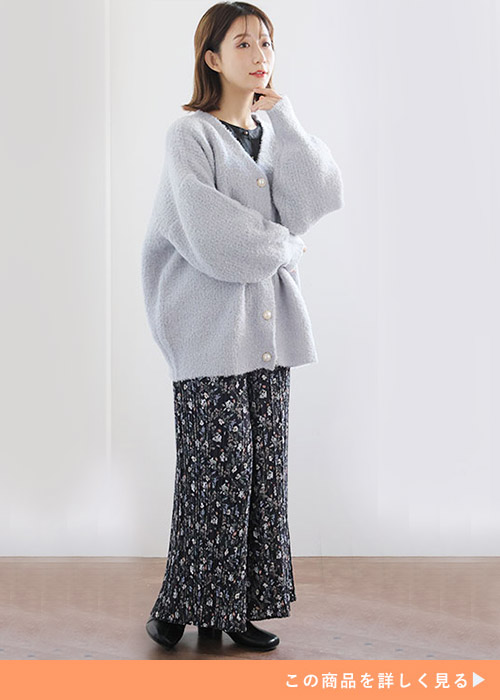 黒トップスにくすみブルーのニットカーデを羽織り、モノトーンの花柄ワイドパンツを履く女性